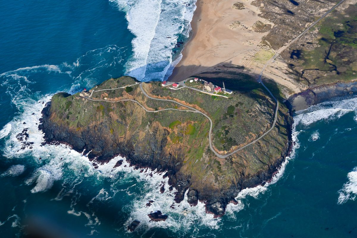 Aerial view of Point Sur, a large volcanic rock with the light station buildings and a winding access road on top
