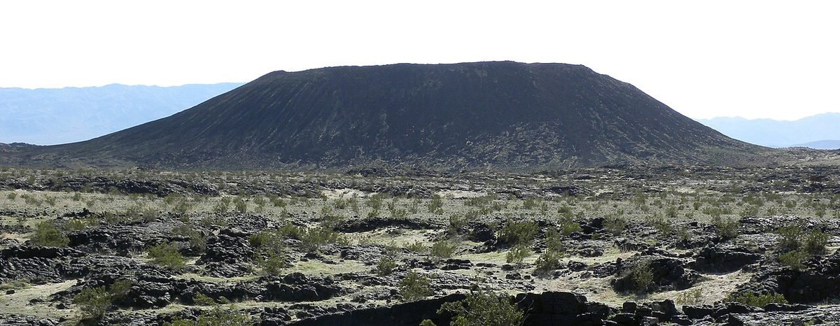 Dark cinder cone of Amboy Crater rising above a desert lava field