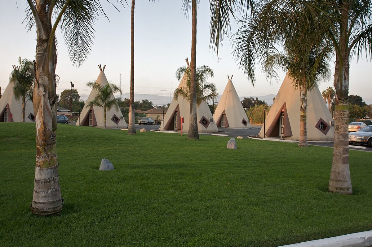 Concrete teepee-shaped motel rooms around a lawn with palm trees at the Wigwam Motel