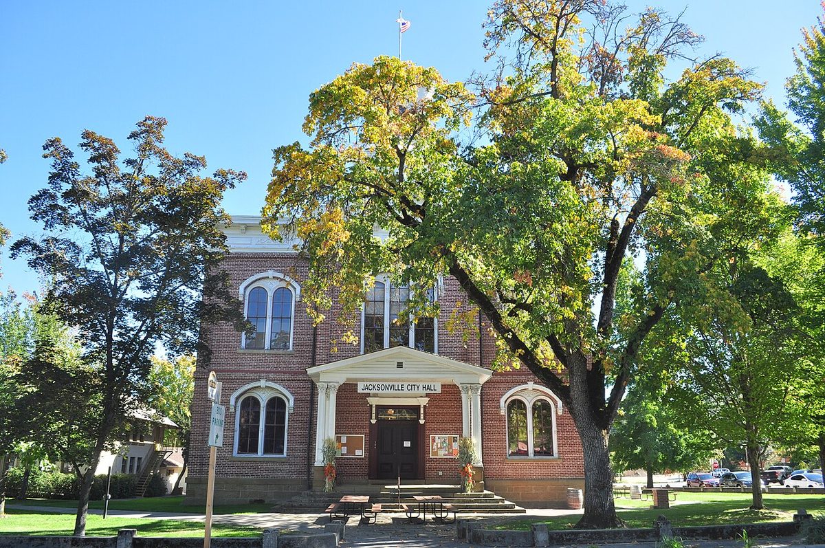 The red-brick former Jackson County Courthouse in Jacksonville, Oregon, behind large trees turning gold