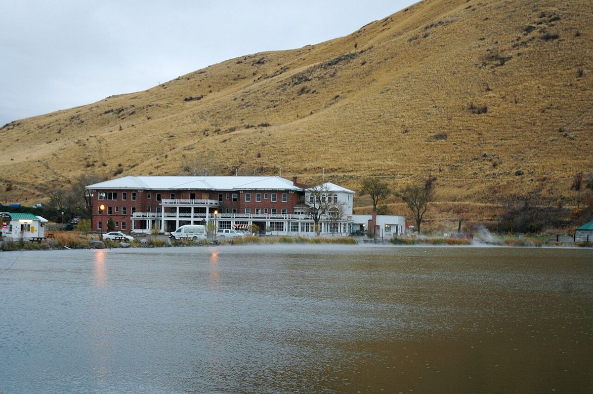 The long brick Hot Lake lodge on the far shore of Hot Lake, with dry hills rising behind it, near La Grande, Oregon