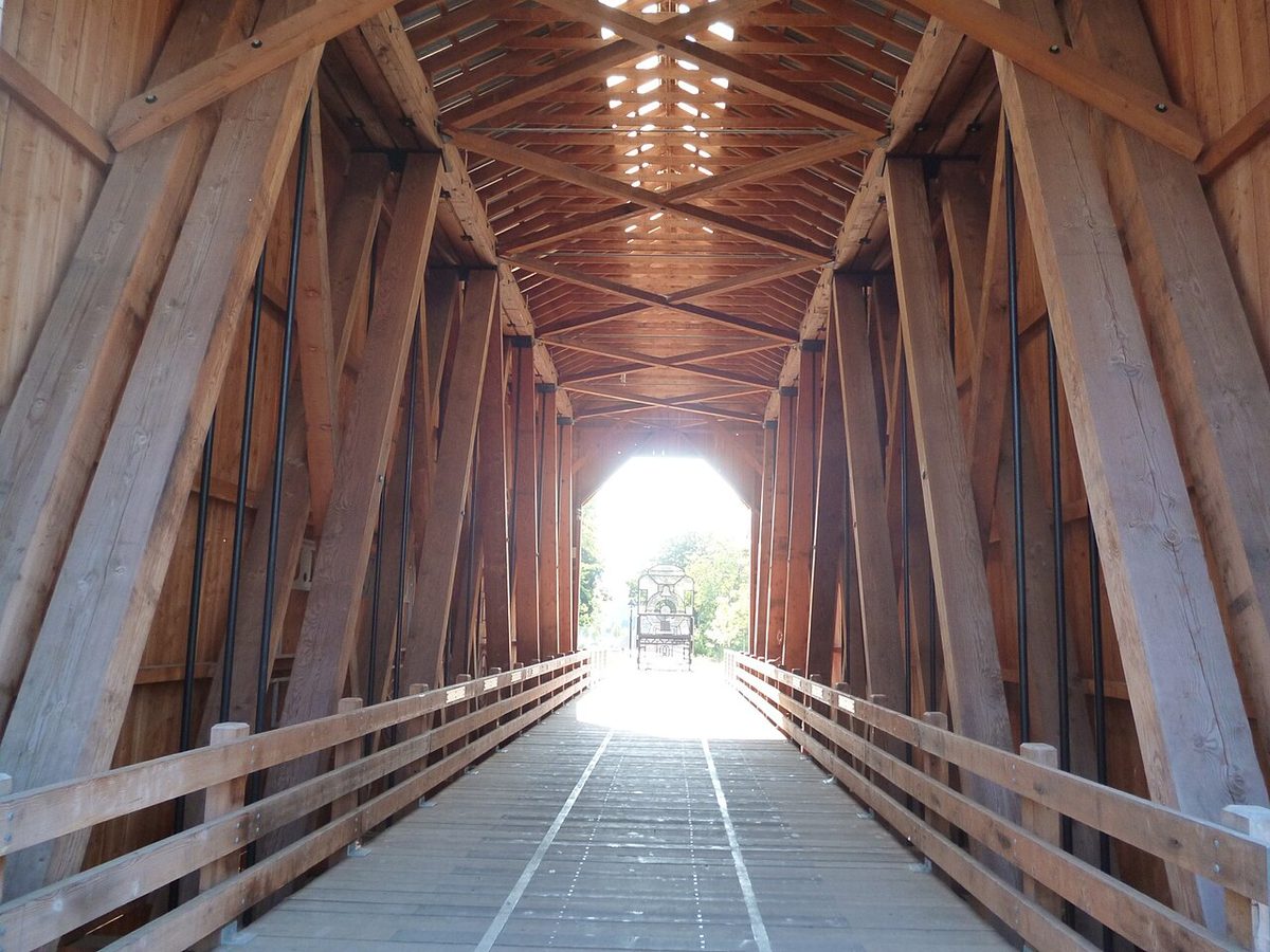 Inside the restored Chambers Railroad Covered Bridge in Cottage Grove, Oregon, with timber trusses framing a pedestrian deck