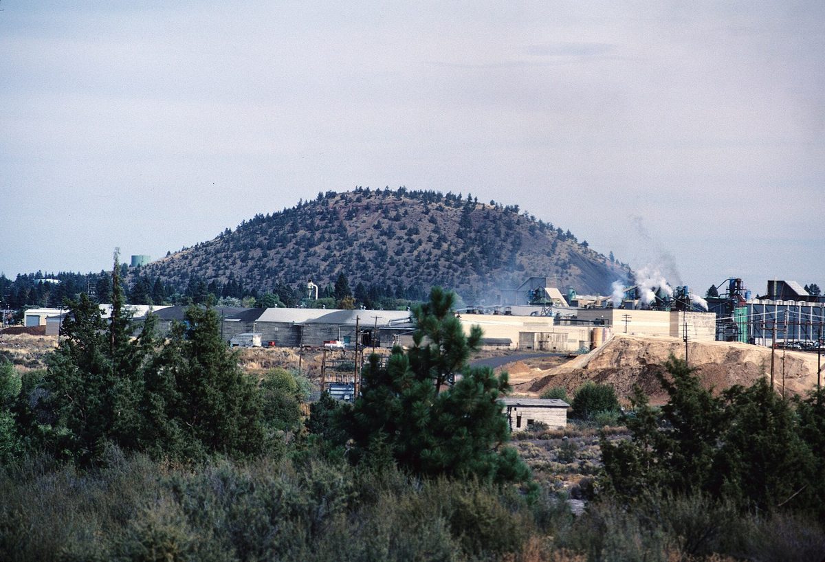 The rounded, tree-dotted cone of Pilot Butte rising behind buildings in Bend, Oregon