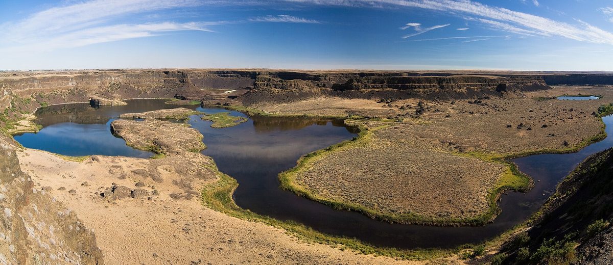 Panorama of the horseshoe-shaped cliffs of Dry Falls curving around small lakes in a dry basalt coulee