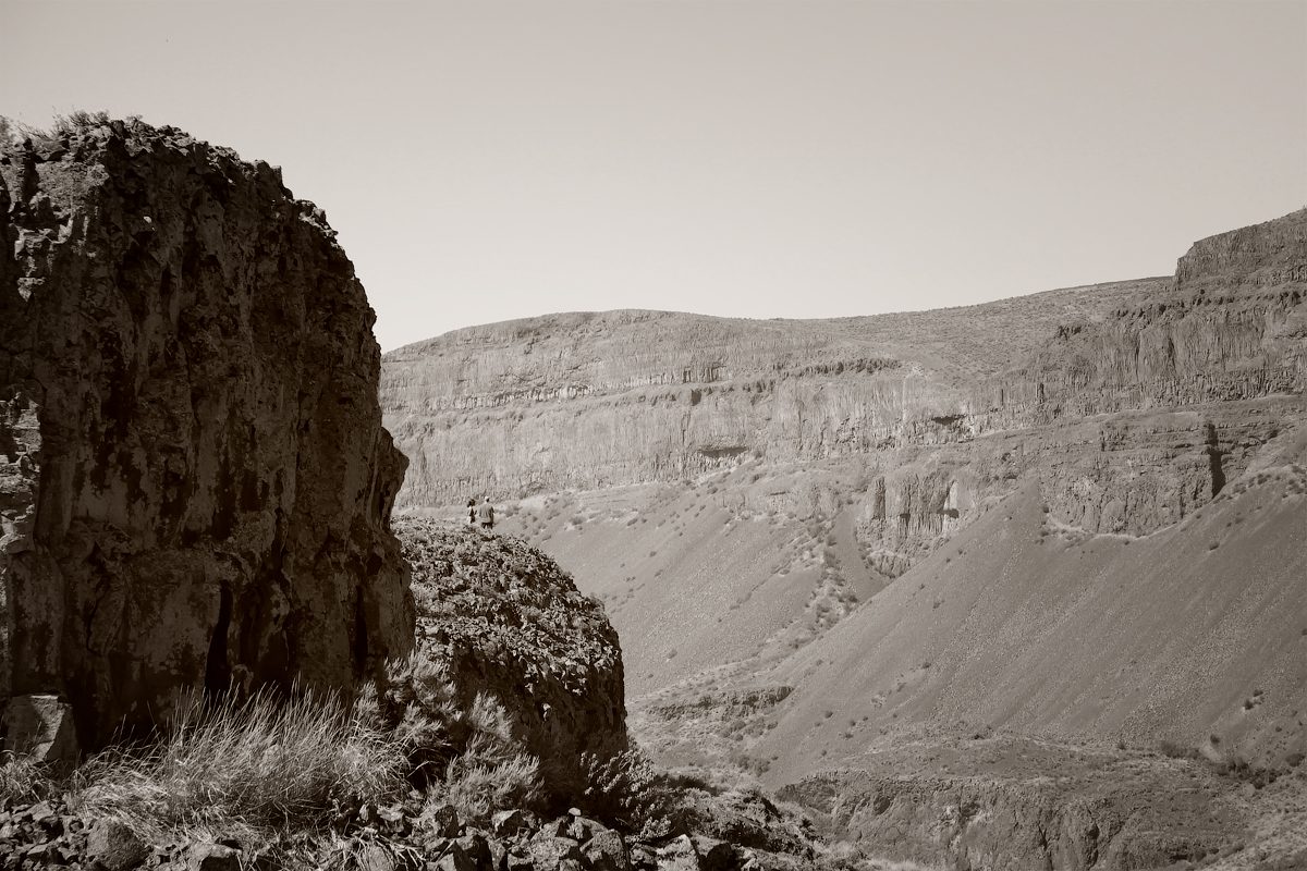 A dark basalt pillar beside the Lake Lenore Caves trail, with the coulee wall and slopes behind